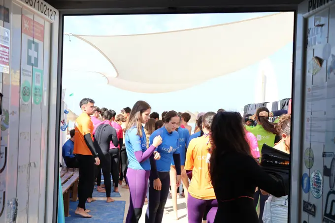 Jovens com lycras da Duck Dive a preparar-se para uma aula à entrada da escola de surf, na praia