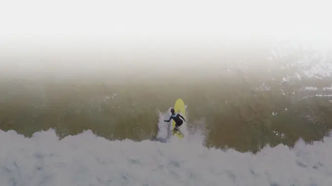 Vista aérea de um surfista numa prancha amarela a contornar a rebentação
