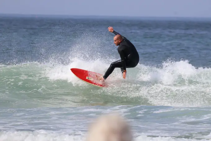 Surfista a descer a parede de uma onda numa prancha vermelha na Praia do Castelo, Costa da Caparica
