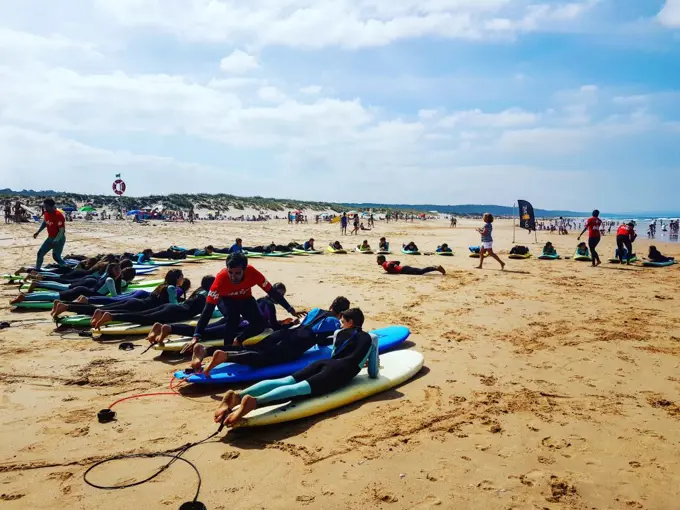Turma de alunos deitada em pranchas soft na areia a treinar o take-off